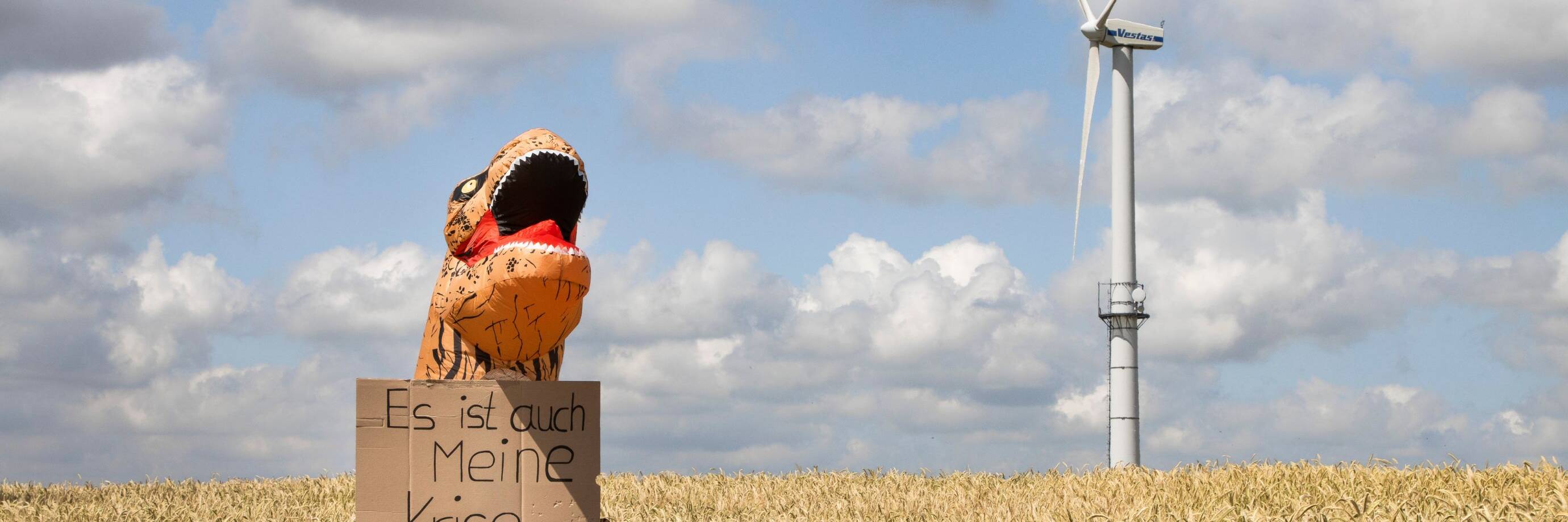 Dino neben Windrad im Feld "Es ist auch meine Krise"