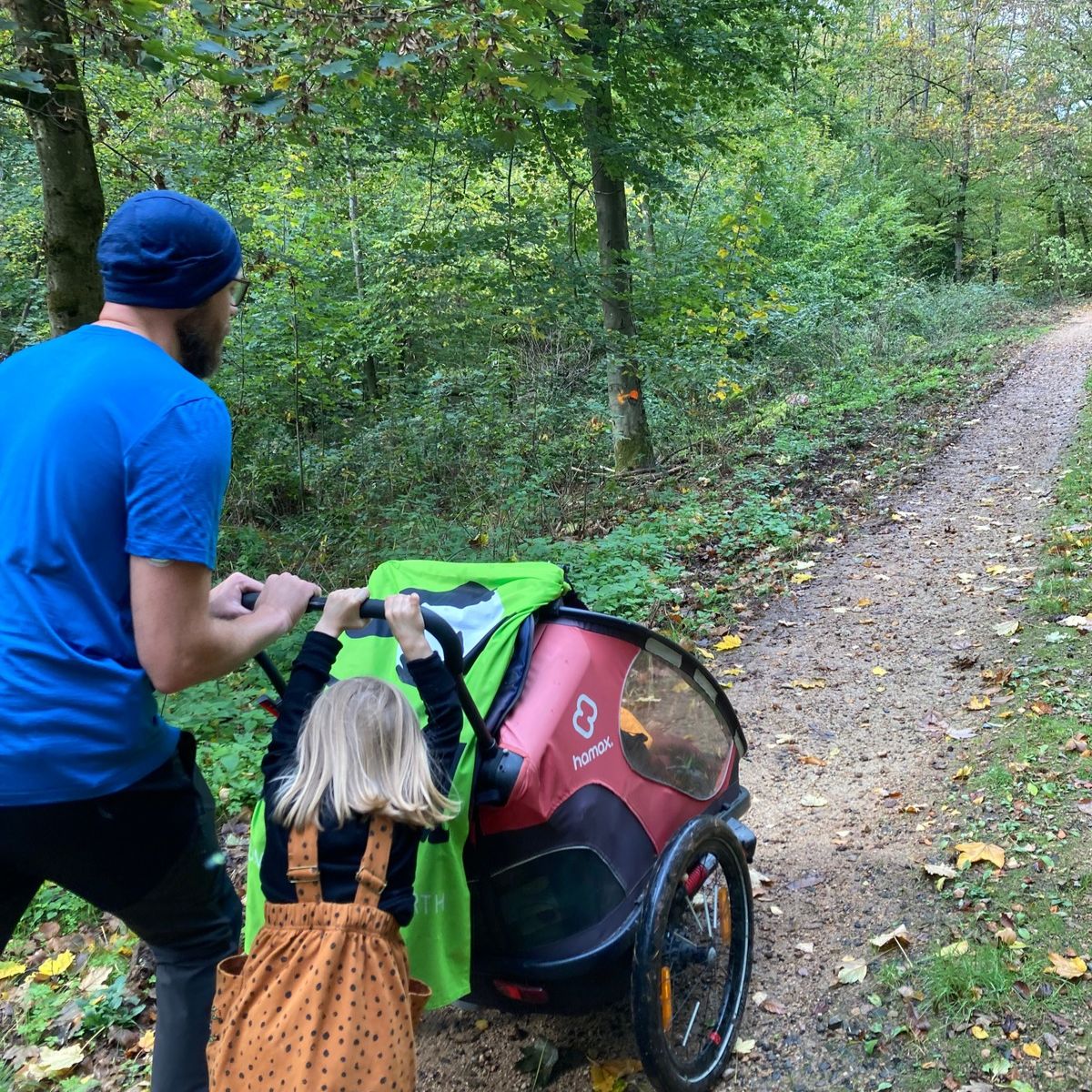 Fahrradhänger wird von zwei Personen einen Waldweg nach oben geschoben
